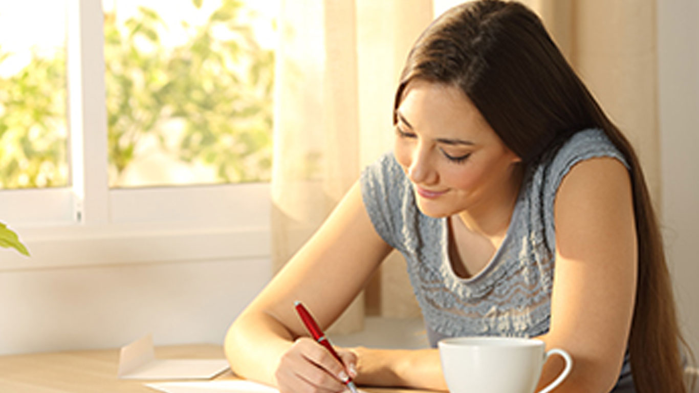 Smiling-Woman-Sitting-at-Table-Writing